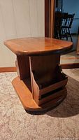Full view of wooden side table showing natural wood top, base, and magazine rack structure on both sides.