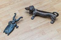 Both cast iron items shown on wooden floor: dachshund door stop and scarab beetle boot jack
