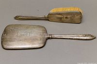 Hand mirror and brush set showing top sides, silver surface with monogram and floral details