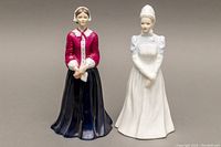 Front view of both porcelain nurse figurines, one in navy and burgundy, the other in white uniform.