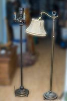 Full view of both metal floor lamps side by side showing bases and upper parts with shade on one lamp.