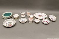 Full set of assorted fine china items arranged showing three reticulated bowls, dessert plates, sugar bowl, creamer, and a floral dinner plate.