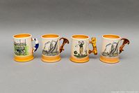 Front view of four ceramic tankards with different sports scenes and decorative handles on a gray background.