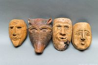 Four old hand carved wooden masks arranged side by side showing both animal and human faces.