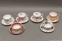Side angle front view of the six teacup and saucer sets arranged in two rows showing the designs and colors