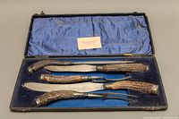 Five-piece carving set inside blue lined fitted case, showing antler handles and sterling silver bands on top and bottom of each handle, along with case interior damage.