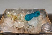 Overview of the crystal and glassware items including various bowls, stemware, blue bottle and glass figurine placed in a cardboard box.