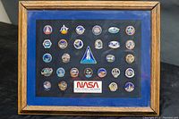 Framed display showing all pins with NASA label and wooden frame.