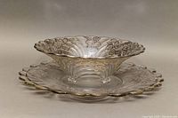 Crystal footed bowl and round serving platter with scalloped edges and sterling silver floral overlay decoration, shown stacked.