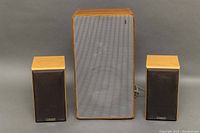 Pair of Mission MS-50 speakers and single Braun speaker arranged upright with grilles on the Mission speakers.