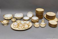 Full set of vintage Limoges and similar Japanese porcelain china with gold gilded rims and monogram E, showing plates, bowls, platters, teacups, creamers, and condiment bowl arranged side by side.