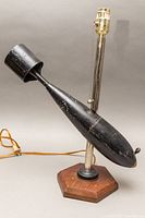 Full view of decommissioned WWI bomb converted into table lamp with wooden hexagonal base and metal lamp fixture showing pull chain and power cord.