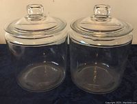 Front view of two clear glass jars with lids on, placed side by side on a dark fabric surface.