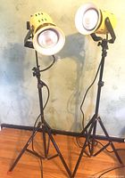 Two yellow Smith Victor Model A50 spotlights on black tripod stands, positioned upright on hardwood floor against a wall, showing full height and body details.