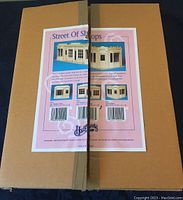 Top view of sealed box with label showing images and information about the Houseworks Street of Shops two window shop kit.