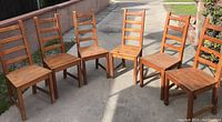 Six solid wood ladder-back chairs arranged on concrete surface outdoors, showing overall shape, size, and condition.