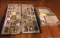 Open binder pages filled with baseball cards in slick plastic sleeves, showing front and back faces of cards including player images and stats.