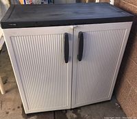 Front view of Black & Decker plastic garden storage cabinet with double off-white doors and black top surface, showing handles and overall condition.