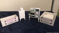 Two white cast iron dollhouse kitchen appliances shown with their boxes; labels read 'Monitor Top Refrigerator' and 'Roper Range'