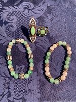 Four-piece set of jade green costume jewelry including two stretch bead bracelets and two rings arranged on dark patterned fabric.