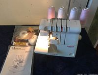 Singer Ultralock 14 overlock machine with four pastel thread cones on spindles, instruction manual and accessory bag visible on table surface.