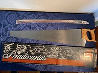 Full view of the Bahco Stradivarius musical saw with its packaging box and A. Breton violin bow wrapped in plastic.