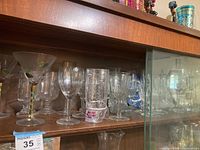 Shelf with multiple stemware glasses of various styles, some etched and some plain.