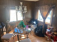 Two brown curtains hanging on metal rods in a corner dining area with table and chairs, showing the fabric, pleats, and general setup.