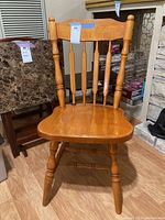 Front view of a wooden chair showing spindle back, turned legs, and wooden seat with scratches.