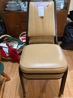 Front view of one beige metal framed stacking chair with padded seat and backrest.