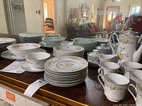 A display of the bulk of the china set showing stacked plates, bowls, cups, and a coffee or teapot with lid.