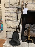 Photo showing the metal fireplace tool set with shovel, brush, and poker on the stand in front of stone fireplace surround.