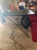 Front angled view of the black folding table showing X-shaped metal legs and rectangular top.