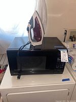 Magic Chef microwave oven with Black & Decker iron placed on top, showing size and condition of both items.