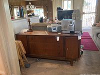 Full view of mid-century modern wood sideboard cabinet with some items placed on top, in a room with carpet flooring.