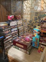 Stack of DVDs and VHS tapes on a table next to boxed puzzles and games.