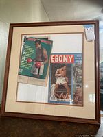 Framed display showing both Sports Illustrated and Ebony magazines featuring Muhammad Ali on their covers, including wear details