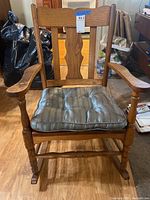 Front view of a wooden rocking chair with cushion showing scratches and wear.