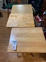 Three wooden snack trays visible, two laid on floor stacked, one standing with legs extended showing folding leg mechanism and wobbly condition.