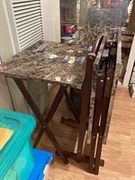 Four folding snack trays with dark marble-patterned tops and wooden stands, stacked and ready to use, showing stickers and residue.