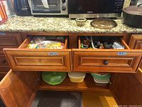 Open kitchen drawers showing plastic storage bags and kitchen utensils inside two wooden drawers under granite countertop.