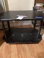 Side view showing the two-tiered structure of the black painted wooden side table with turned spindle legs and surface scratches.