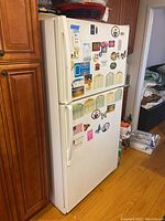 Full front view of the white Whirlpool refrigerator showing top freezer and bottom fridge doors with magnets and notes attached.