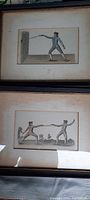 Photo showing two framed antique sword fighting pictures under glass with light matting, each measuring approximately 8" x 6".