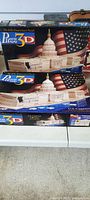 Two boxes of U.S. Capitol Building 3D Puzzle Kits with American flag background on the packaging, showing images of the unbuilt kits.