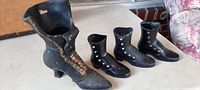 Four antique decorative boots: one large black boot about 10 inches tall with brown laces and three smaller black boots with metal buttons on side