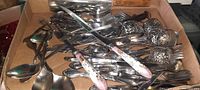 Box with assorted flatware including forks, spoons, knives and decorative handle pieces.