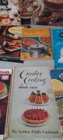 Photo showing various vintage cookbooks including 'Creative Cooking Made Easy' with food cover photos, Mubro-Matic pressure cooker booklet, and others