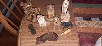Tabletop view of a dozen antique dog figurines in different sizes and materials, arranged closely showing paint detail and textured finish on wood table.