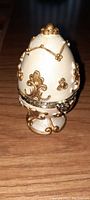 Closed view of vintage cream-colored ceramic egg with gold decorative embellishments and hinged lid